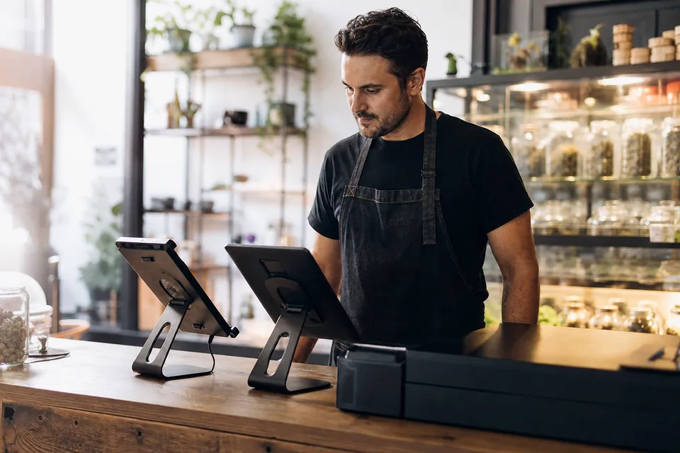Dispensary owner comparing two point of sale tablets side by side on a retail counter